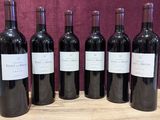 six bouteilles de vin rouge sont alignées sur une table en bois