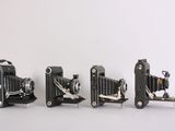 three old cameras sitting side by side on a white surface