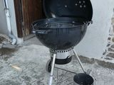 un barbecue noir posé sur le béton devant une maison