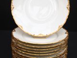 une pile de six assiettes blanches et dorées posées sur une surface noire