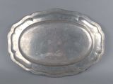 an oval silver tray with a decorative edge on a gray surface