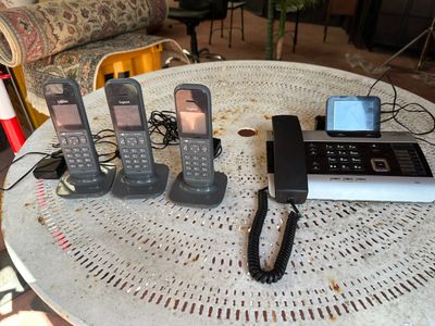 five cell phones sitting on a table with a cell phone plugged to it