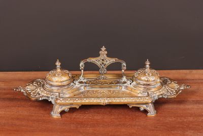 une image représentant un encrier en argent et en or posé sur une table en bois