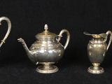 three silver teapots and two silver vases on a black background