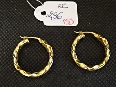 deux boucles d'oreilles en anneau dorées et une étiquette de prix posée sur une surface noire