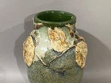 a green vase with leaves on it sitting on a table
