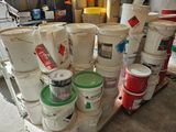 several buckets of paint are stacked on a pallet in a garage