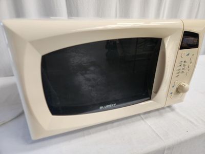 a white microwave sitting on a table with a white curtain behind it