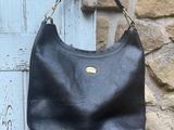 un sac à main en cuir noir accroché à un mur en pierre devant une porte bleue