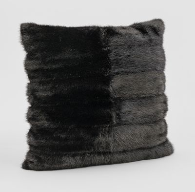L'oreiller en fourrure noire et grise repose sur une surface blanche