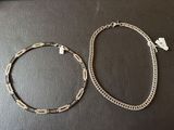 two pieces of silver necklaces on top of a black table