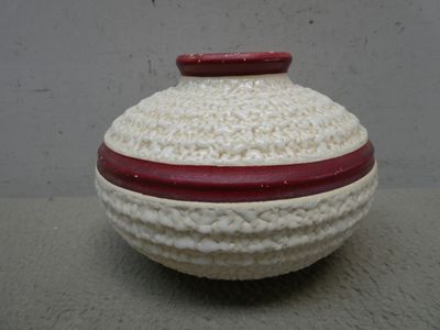 un vase blanc au crochet, muni d'un couvercle rouge, posé sur une table