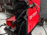 une soudeuse rouge dans un garage, avec une boîte posée par terre