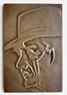 une plaque en bronze représentant un homme coiffé d'un chapeau et portant une moustache