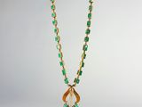 un collier composé de perles vertes et dorées et d'un pendentif en forme de feuille