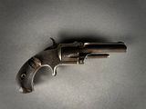 Un vieux pistolet est posé sur une table devant un fond gris.