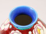 a red vase with a blue rim and flowers on it