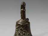 une vieille cloche en bronze posée sur une surface blanche, avec un fond gris
