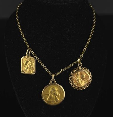 a gold plated necklace with three charms on a black mannequin