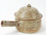 un petit pot marron muni d'une anse, posé sur une surface blanche