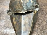 un gros plan d'un masque métallique posé sur une surface marron