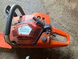 une tronçonneuse orange posée par terre à côté d'une paire de chaussures
