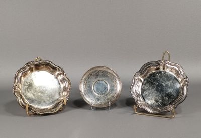 trois plats plaqués argent posés sur des supports, disposés sur une surface grise