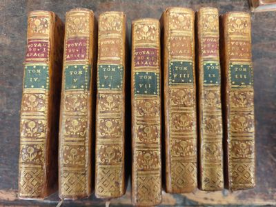 Six vieux livres sont alignés sur une étagère à côté d'une bibliothèque.