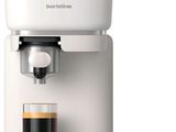 La machine à café est blanche et il y a une tasse de café devant elle.