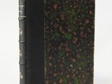 an old book with a black cover sitting on top of a white surface