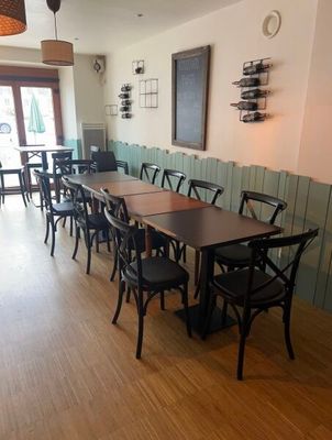Dans un restaurant au sol en parquet, des tables et des chaises sont alignées.