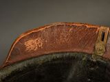 brown leather hat with brass buckles on top of a black hat