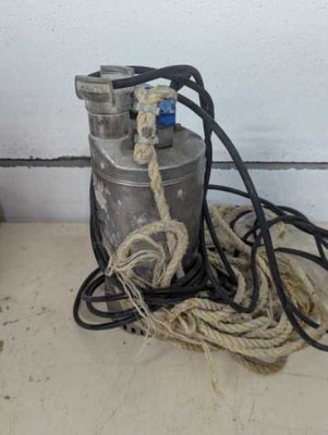 un fût métallique attaché à une corde, posé par terre près d'un mur