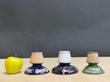 three different colored candlesticks sitting on a table with an apple in the background