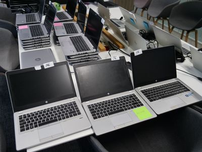 Plusieurs ordinateurs portables sont alignés sur une table dans une pièce.