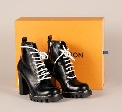 une paire de bottes en cuir noir avec des lacets blancs et une boîte