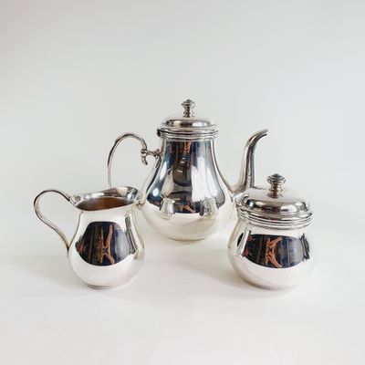 three pieces of silver tea and coffee set on a white surface