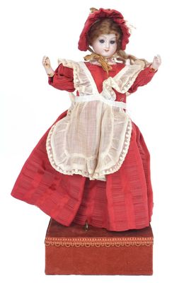 une poupée vêtue d'une robe rouge et d'un bonnet, assise sur une boîte