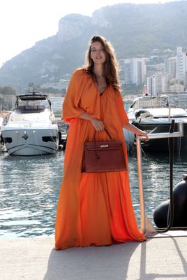 une femme en robe orange, debout au bord de l'eau
