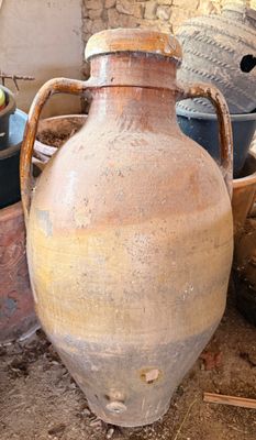 un grand vase marron posé par terre à côté d'autres pots