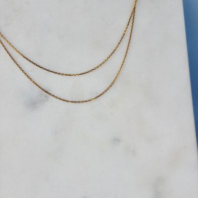 un collier à chaîne en or posé sur une dalle de marbre