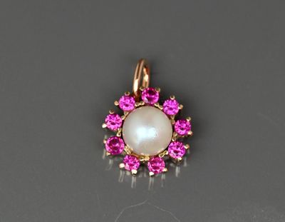 Gros plan sur un pendentif composé d'une perle et d'un saphir rose, posé sur une surface noire