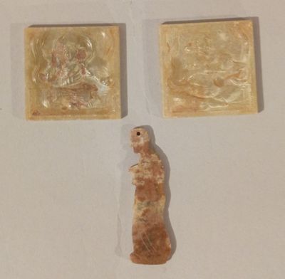 Trois œuvres d'art sont exposées sur une surface blanche ; l'une d'entre elles représente une femme et une autre un homme.