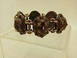 bracelet doré et marron posé sur un socle en acrylique transparent, sur fond blanc