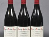 three bottles of red wine are lined up on a gray surface