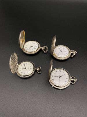 quatre montres de poche en argent posées sur une surface noire