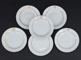 six assiettes blanches aux bords dorés reposent sur une surface noire
