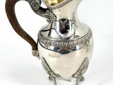 an antique silver pitcher with a wooden handle on a white background