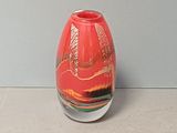 un vase rouge posé sur une table, avec un mur gris en arrière-plan