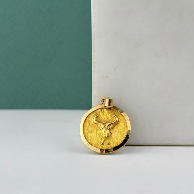 un collier en or orné d'une pièce d'or, posé sur une surface blanche